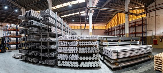 Chapas e barras de alumínio industrial empilhadas em galpão de distribuidora, tons metálicos acinzentados, iluminação industrial neutra, foco nítido nas texturas do metal, fotografia realista de produto